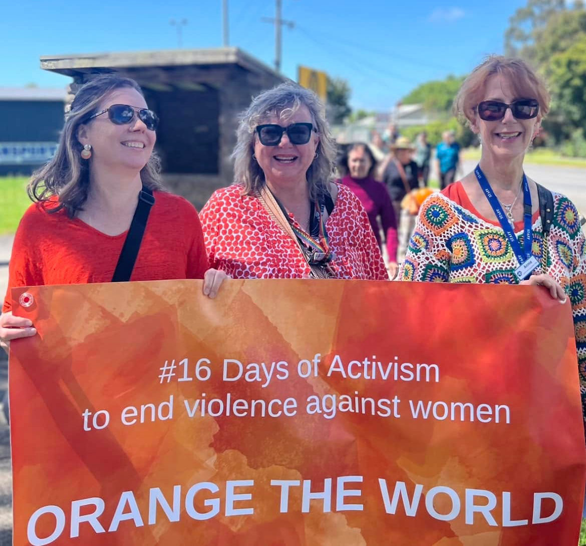 A sunny day with three women holding a sign during a march for #16 days of activism to end violence against women.