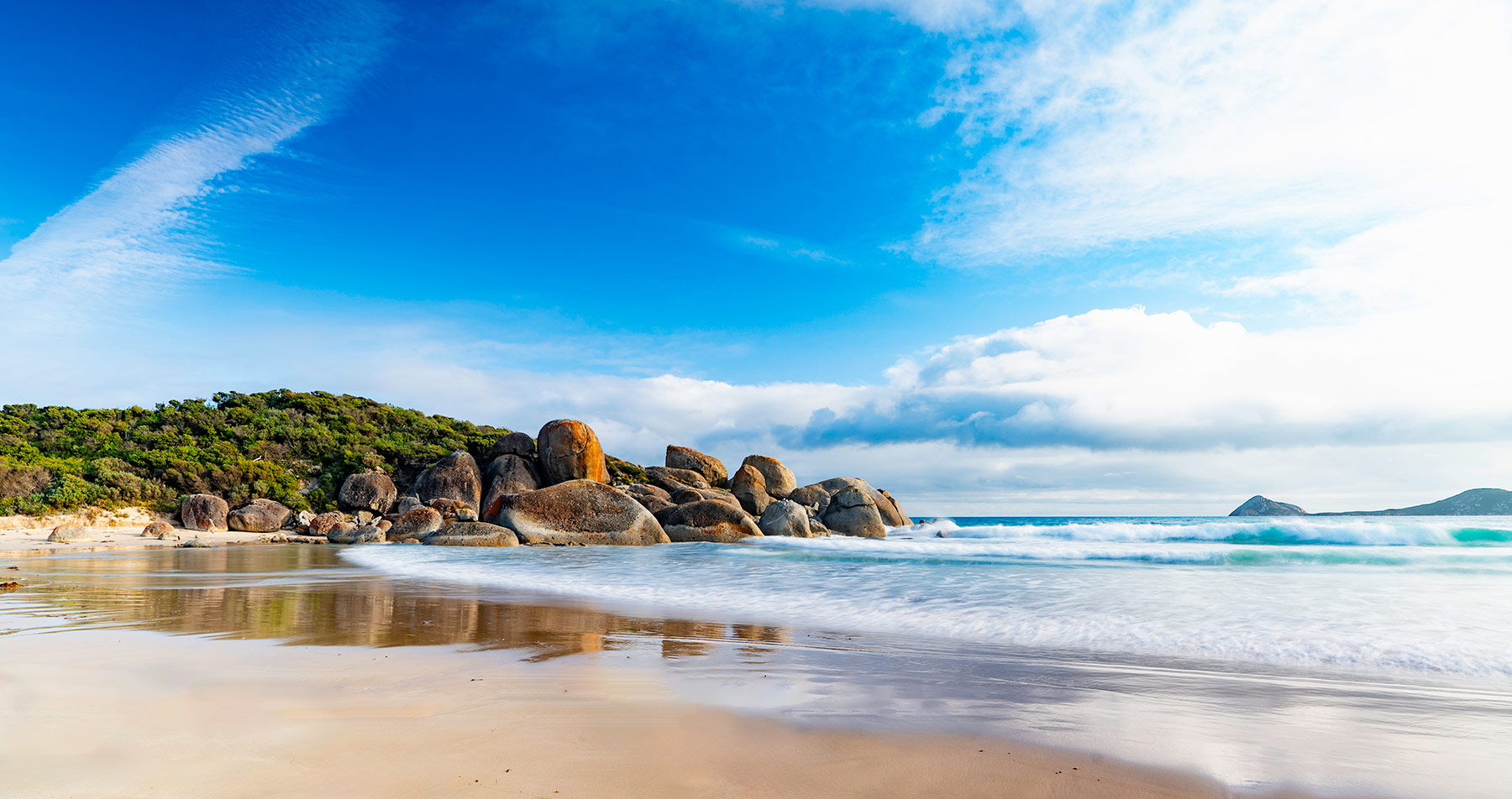 Beautiful Whisky Bay at Wilsons Promontory, showing the surf coming in on the white sandy beach, and some large rocks and native vegetation.