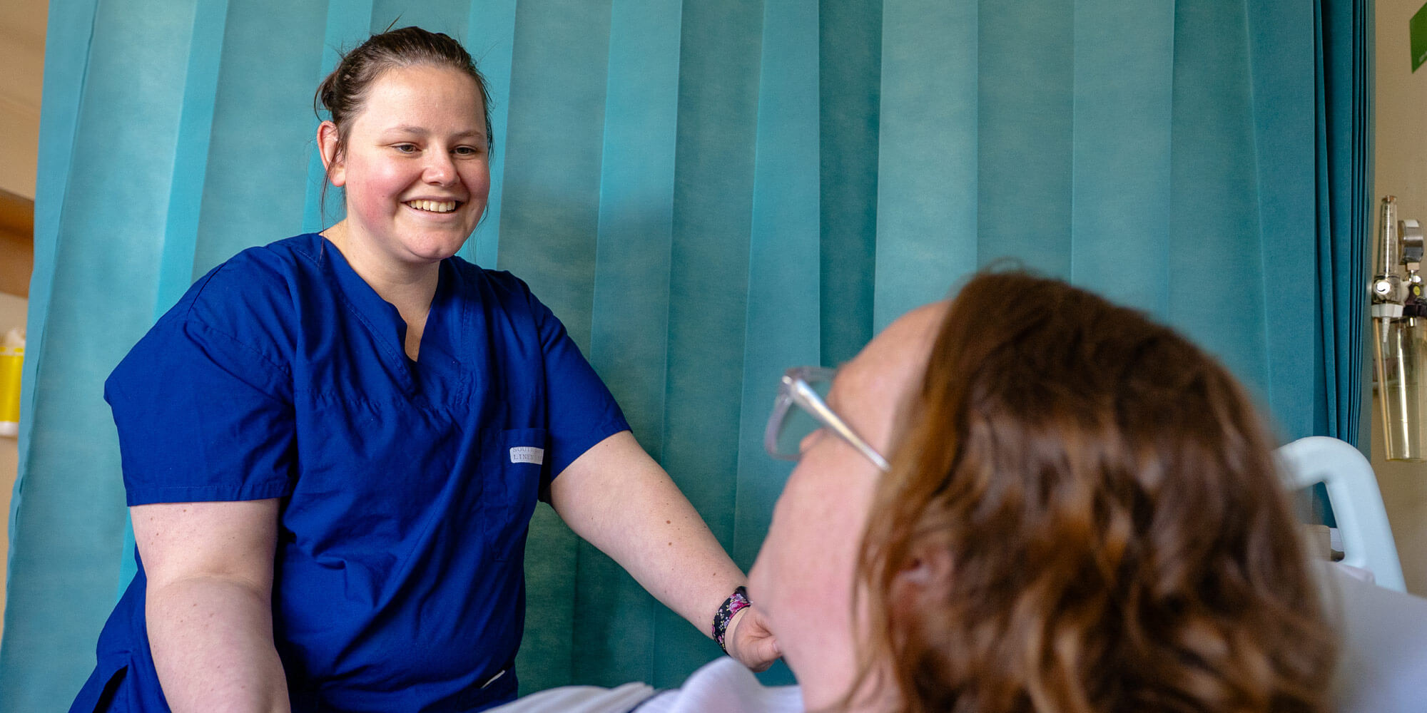 Female nurse assisting a pregnant woman as she lies in bed.