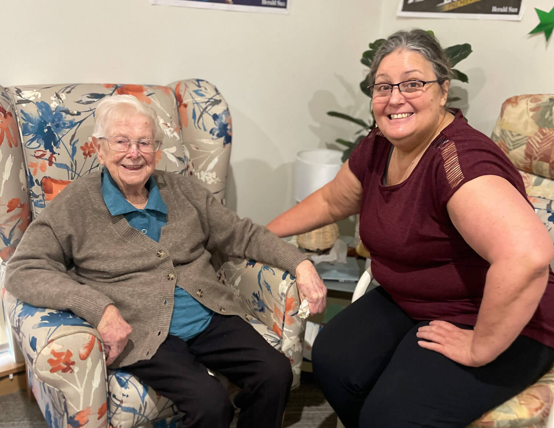 Two ladies, one elderly, sititng in armchairs enjoying conversation.